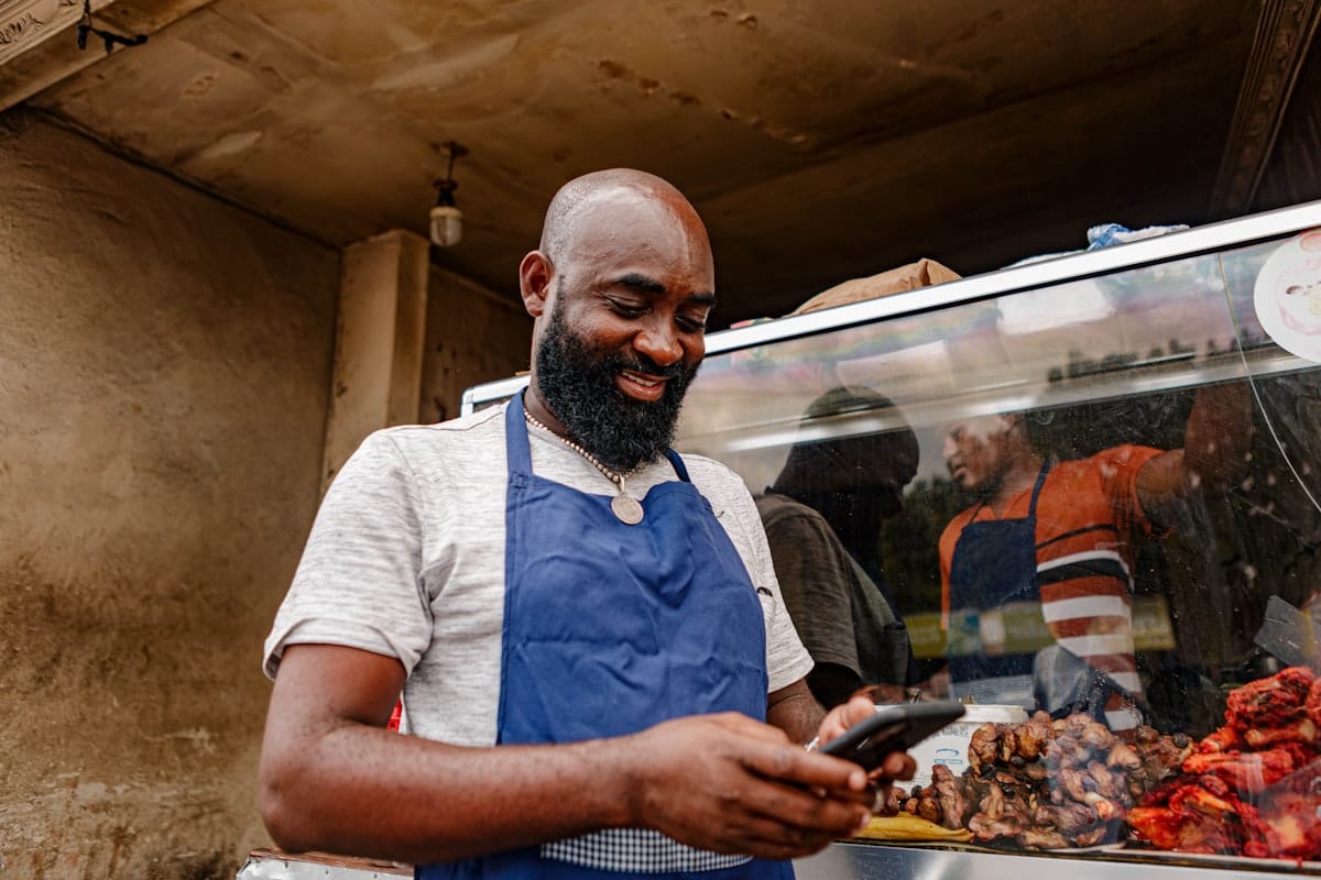 Un artisan en tablier consulte son téléphone pour vérifier sa fiche Google et ses avis clients devant son atelier.