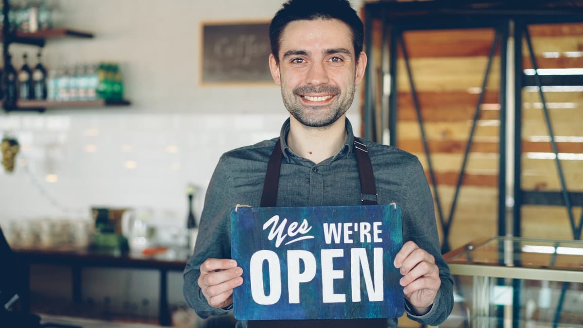 Une personne tient un panneau Open pour accueillir les premiers clients d'une activité qui vient de démarrer.