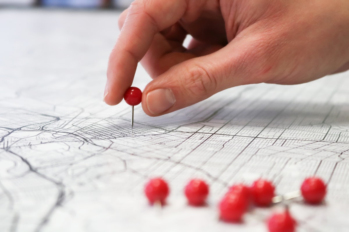 Une personne place une épingle rouge sur une carte de ville, illustrant la zone d'intervention d'un artisan.